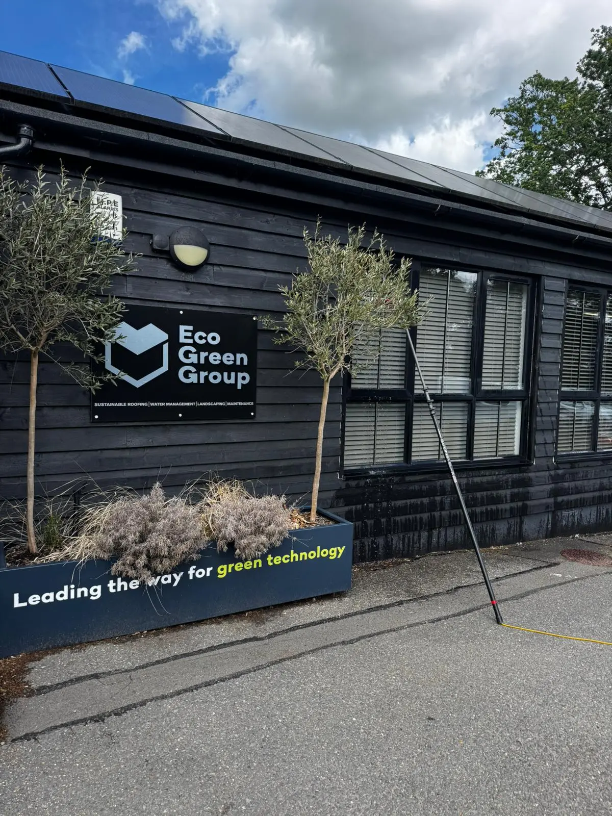Eco Green Group black timber-clad office with solar panels and a water-fed pole
