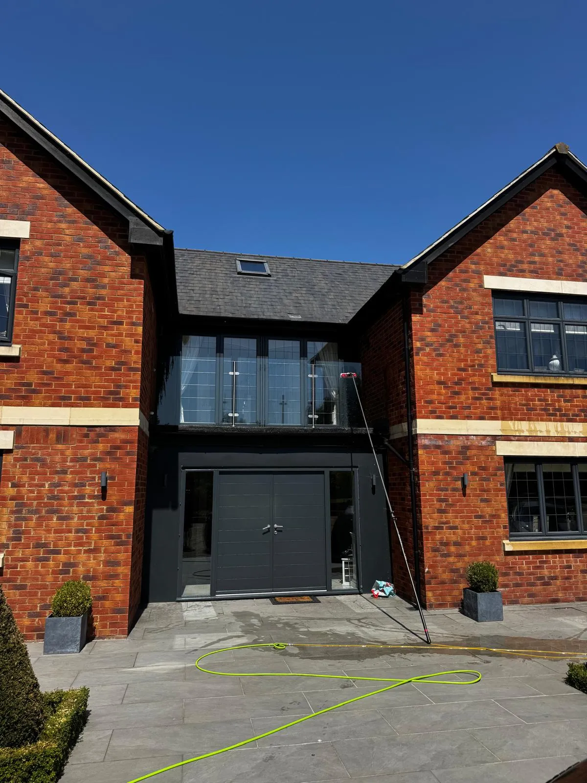 Rear elevation of a modern red-brick new-build home with anthracite windows, cleaned with a water-fed pole from the patio