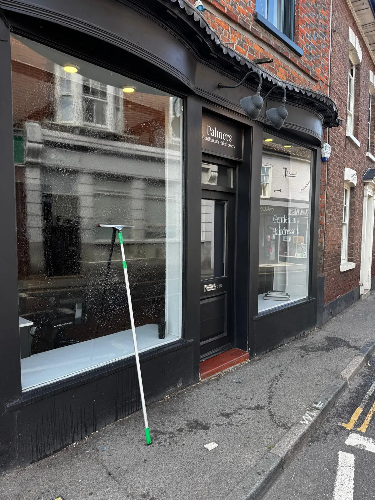 Black-framed shopfront of Palmers Gentleman's Hairdressers on a high street, with a squeegee resting against the freshly washed display window