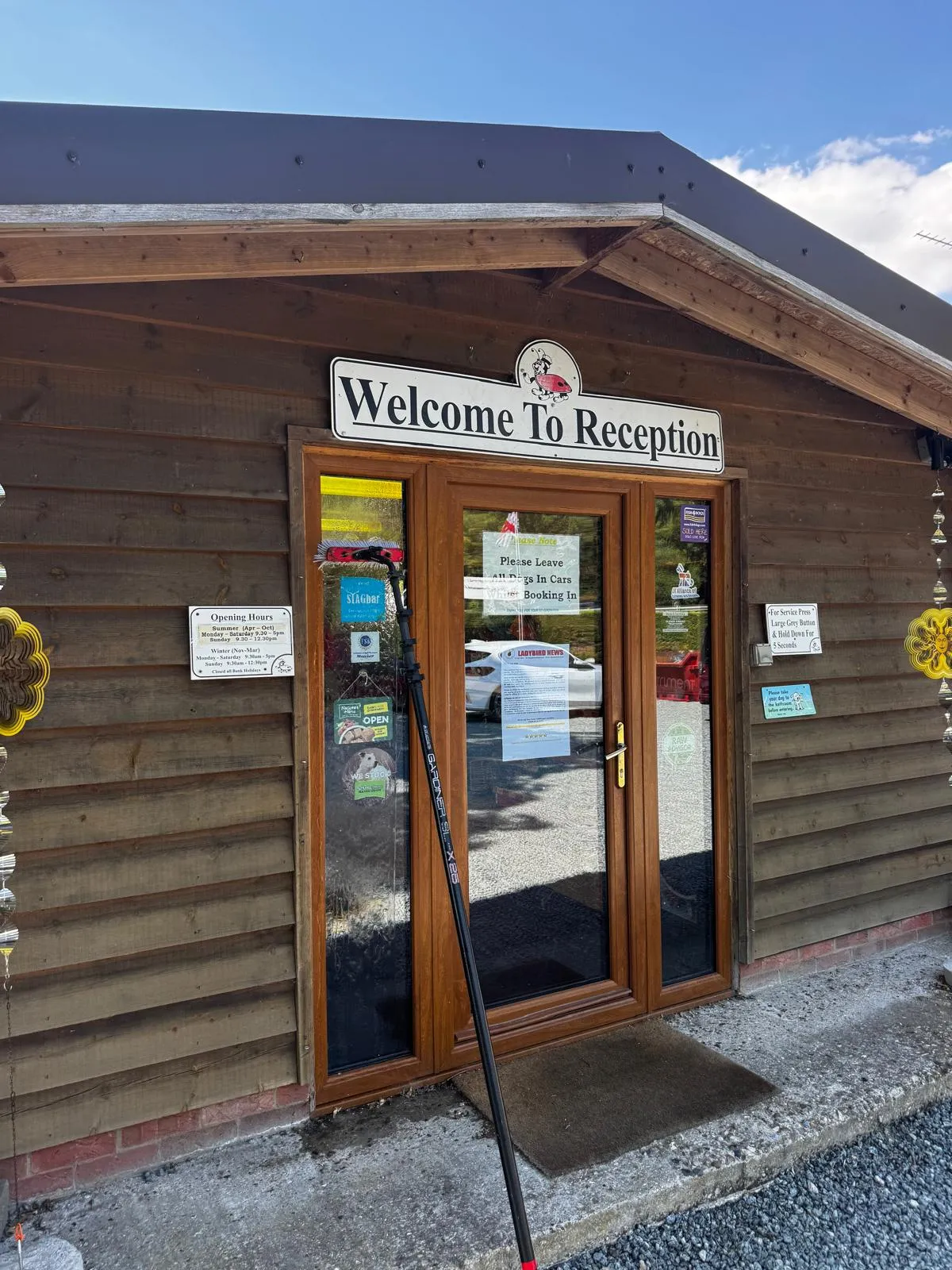 Timber-clad holiday park reception building with a Welcome To Reception sign, its glazed entrance doors being cleaned with a water-fed pole