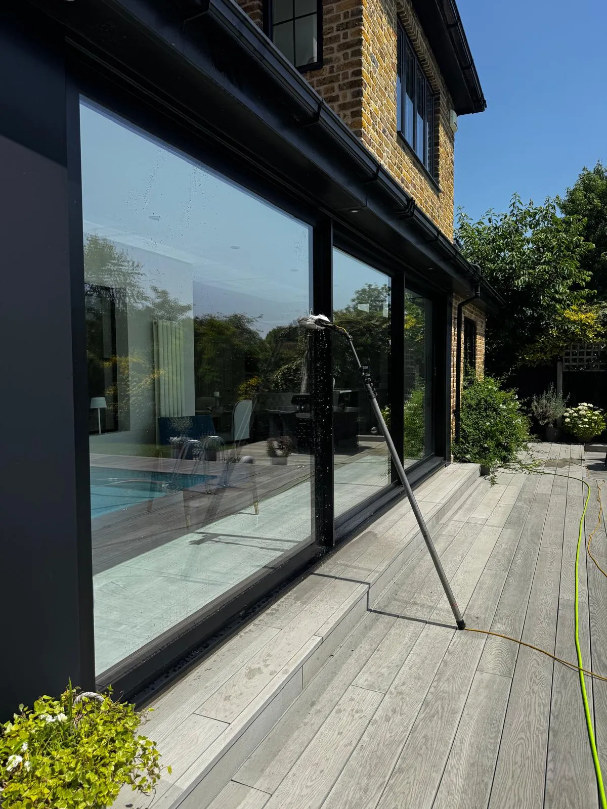 Large black-framed sliding glass doors on a brick family home being cleaned with a water-fed pole beside grey decking