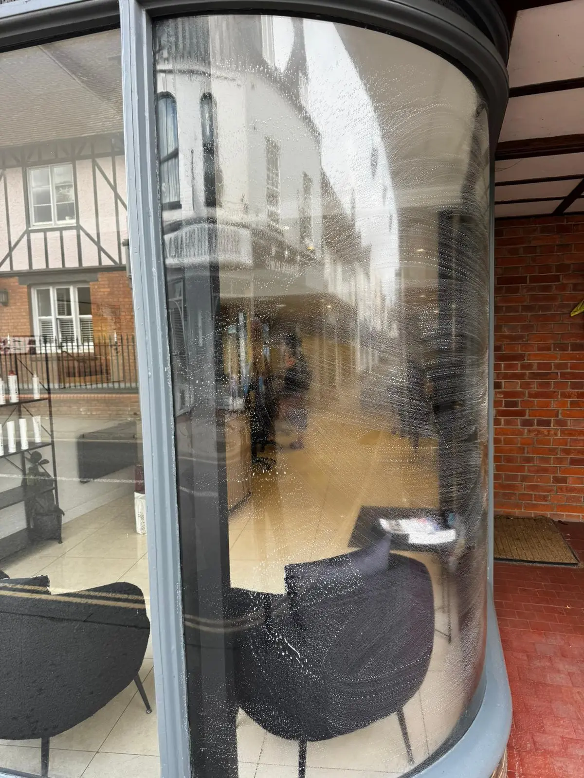 Curved feature shopfront window being cleaned, reflecting the high street